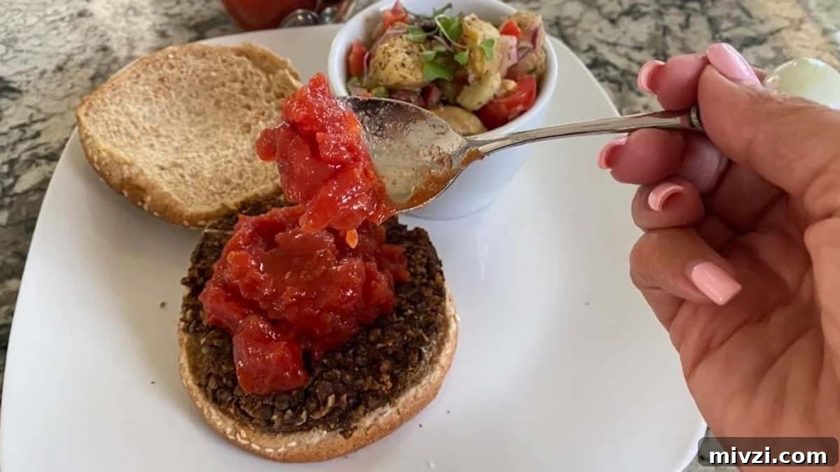 I am adding savory jam to a lentil burger on a plate with a side of vegan potato salad. 
