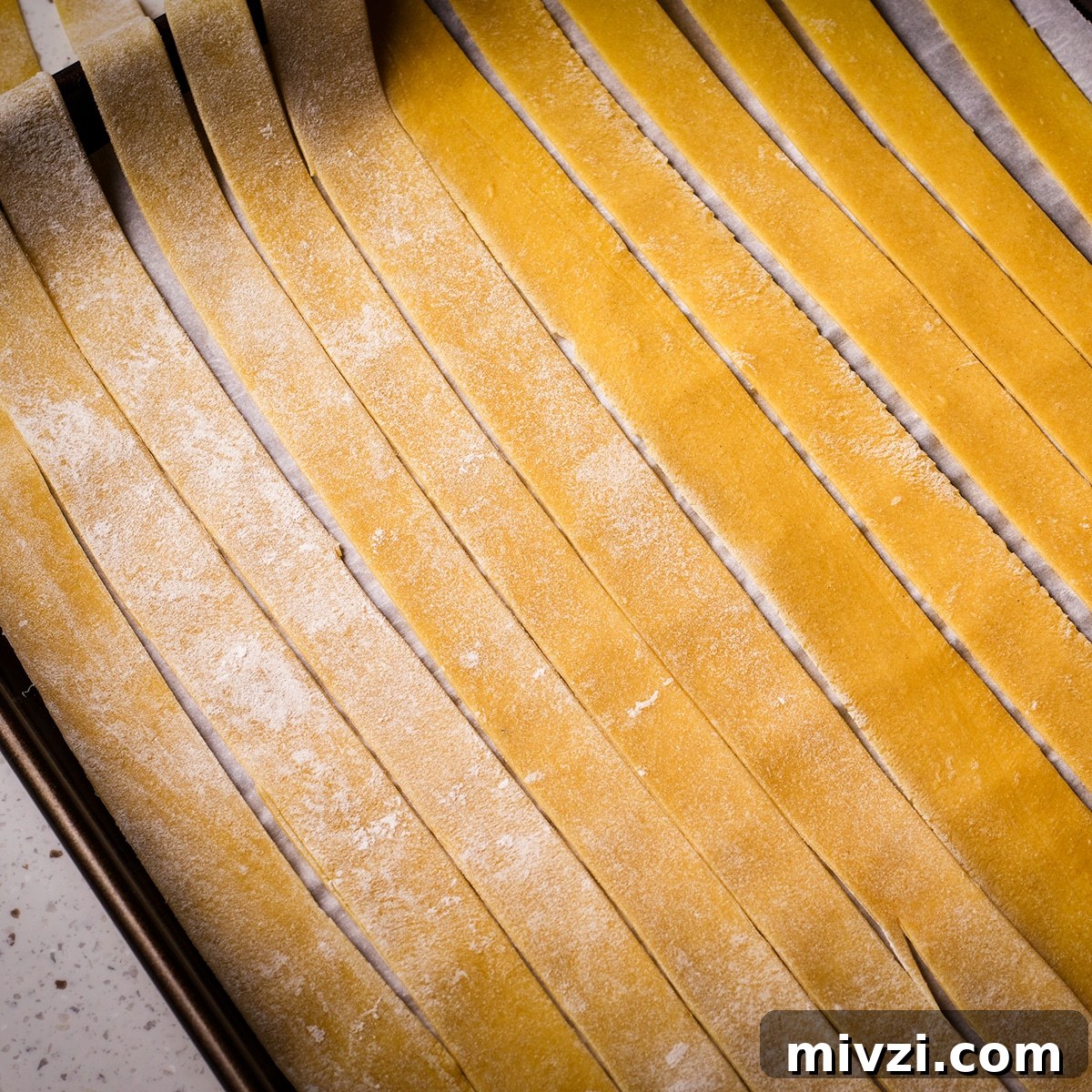 Homemade Pappardelle Recipe: Fresh Pasta from Scratch 20 Homemade pappardelle noodles laid out across a parchment paper lined baking sheet.