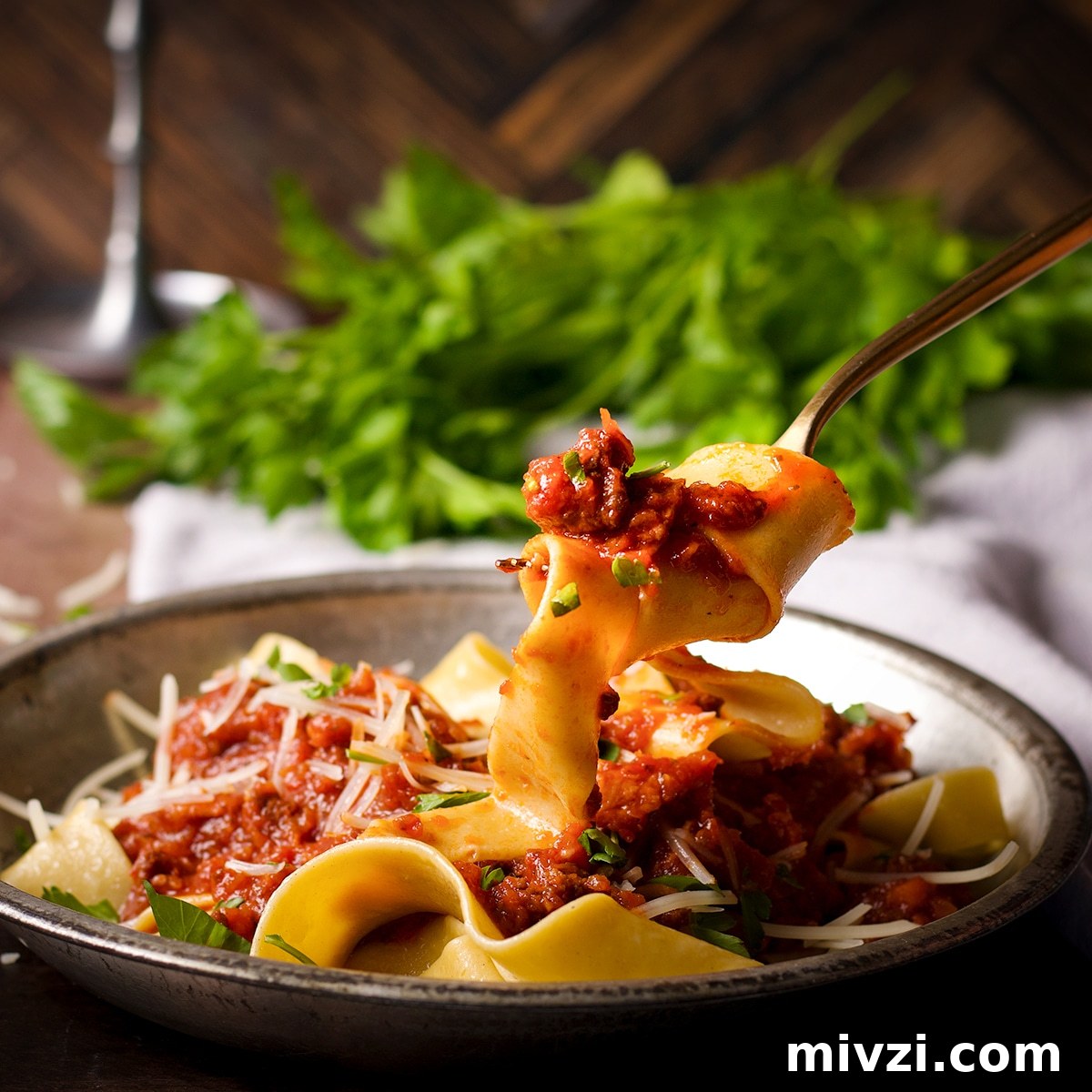 Homemade Pappardelle Recipe: Fresh Pasta from Scratch 3 Using a fork to lift a pappardelle noodle covered in bolognese sauce from a plate.
