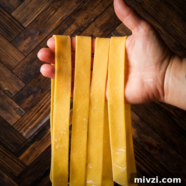 Holding up several homemade pappardelle noodles .