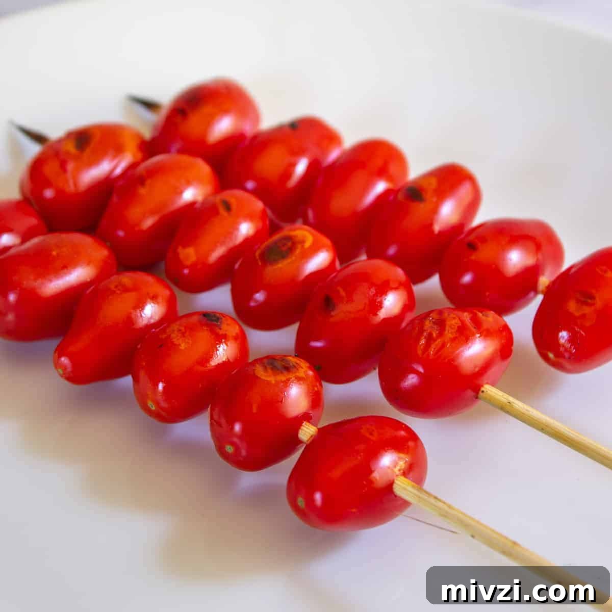 Oven-Roasted Cherry Tomatoes with Garlic and Herbs 2 Skewered grilled cherry tomatoes on a white plate.