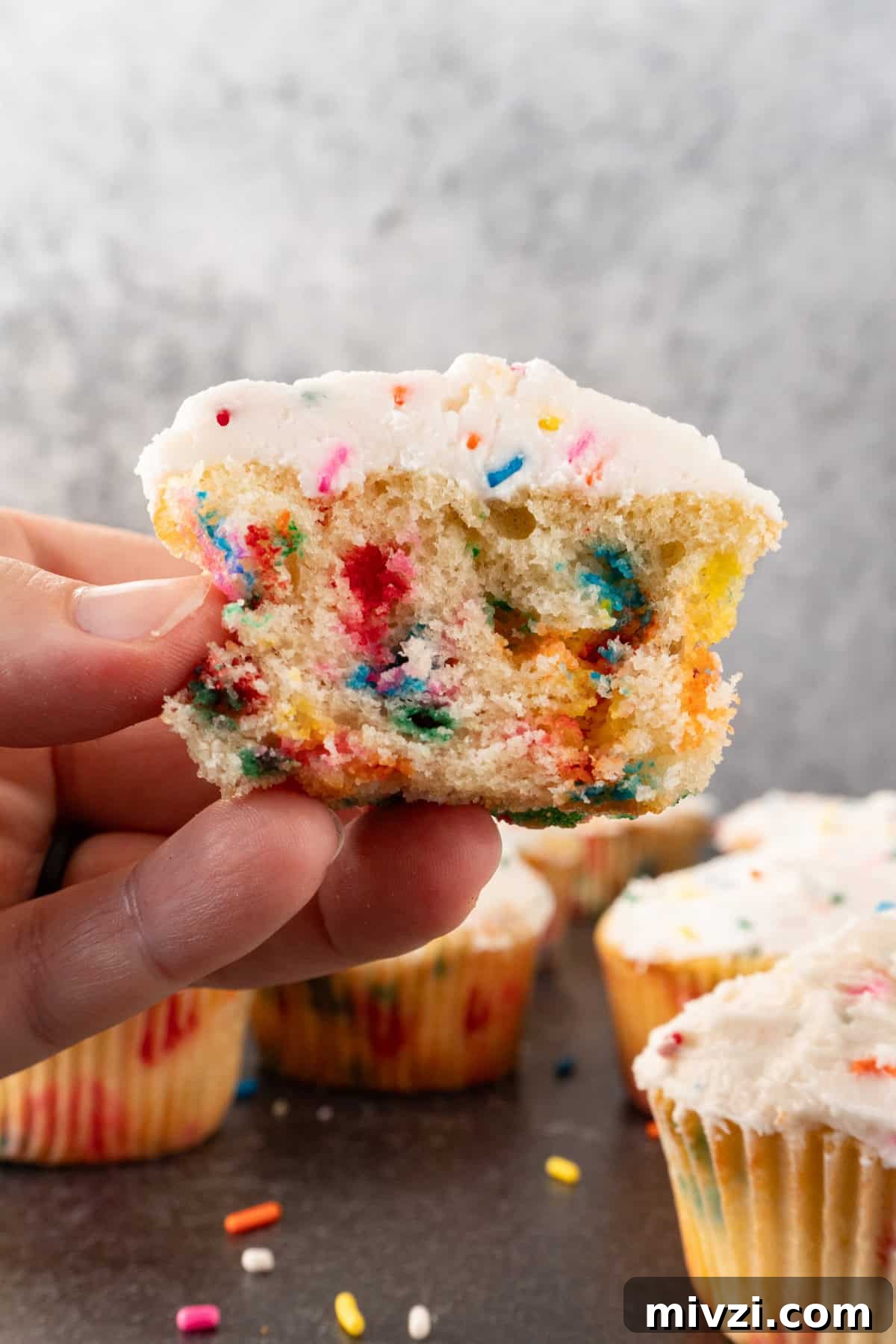 Delicious Birthday Cupcake Recipes for Any Celebration 3 holding a birthday funfettie cupcake cut in half.