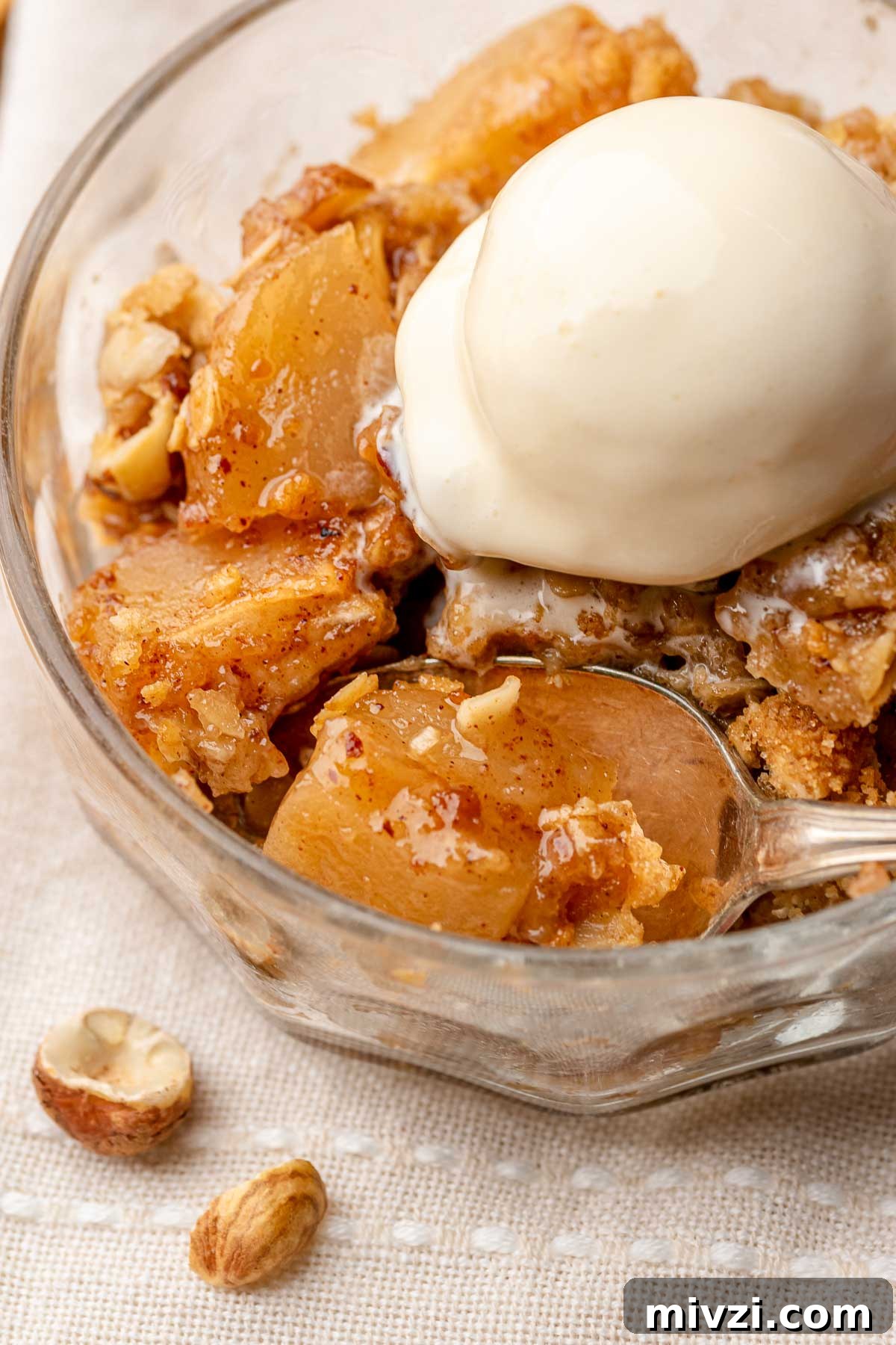 Toffee apple hazelnut crumble in a bowl with ice cream on top and a spoon in the bowl.