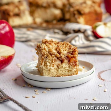 Slice of apple streusel coffee cake on a plate with the rest of the cake in the background.