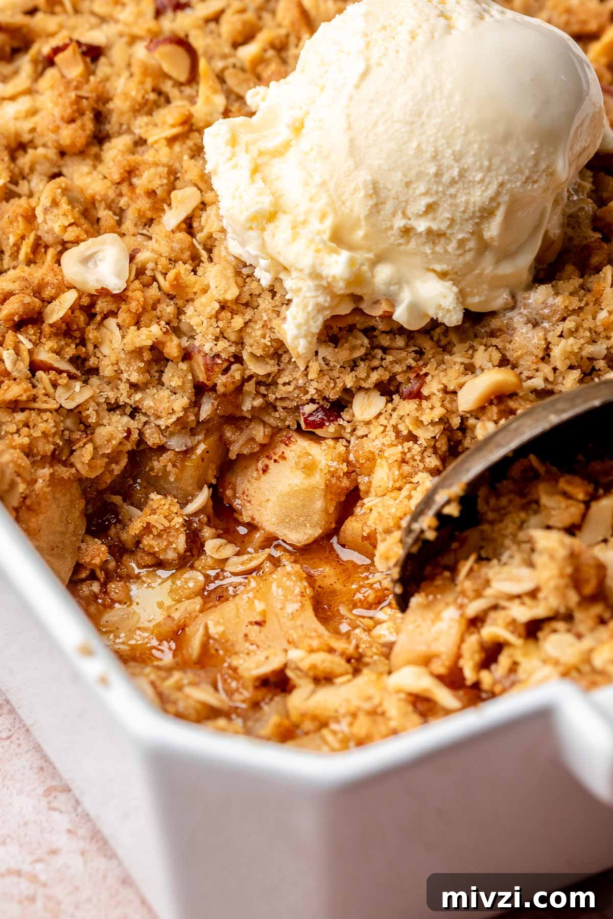 A spoon scoops toffee apple crumble from a casserole dish.