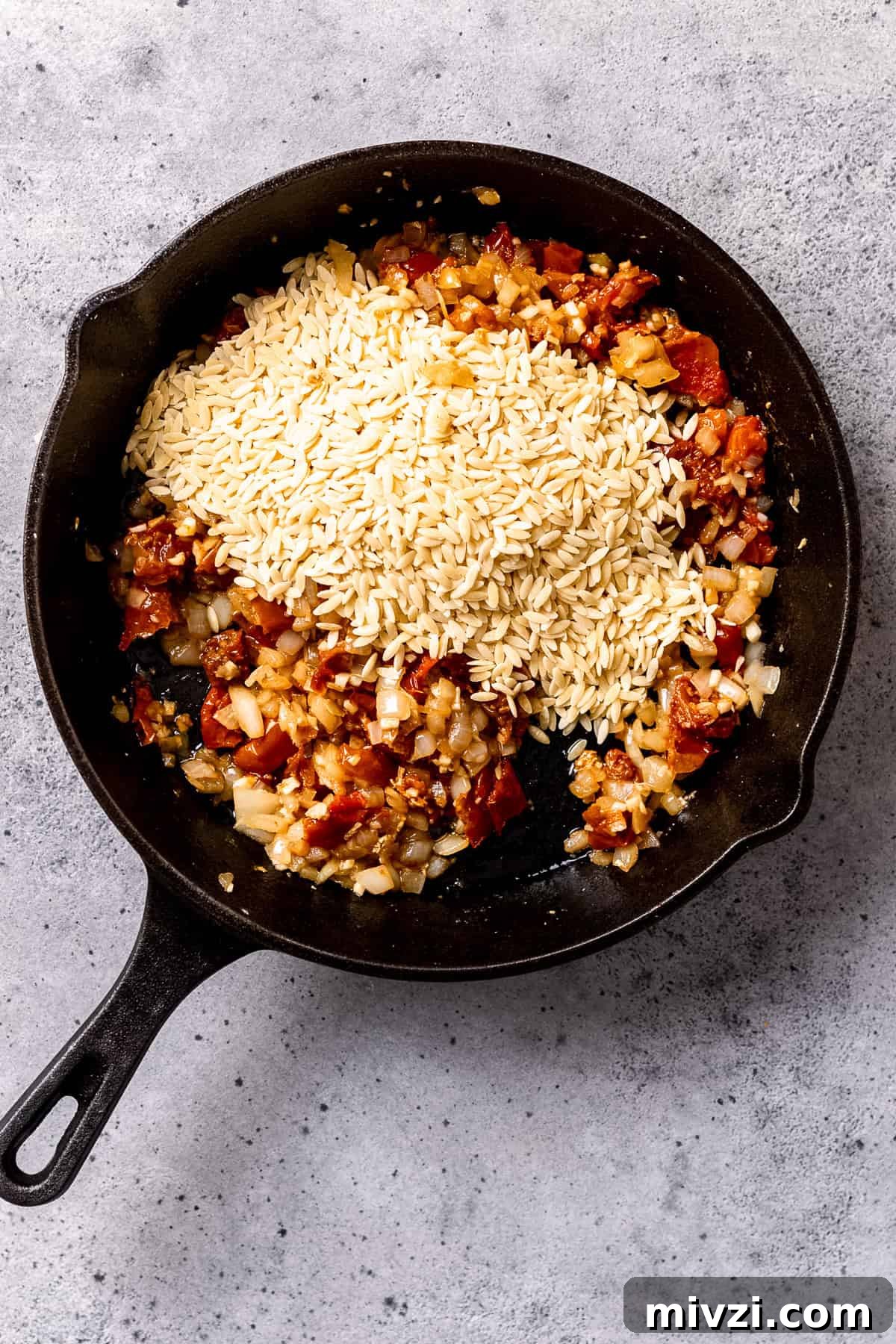 Dried orzo being added to the pan.