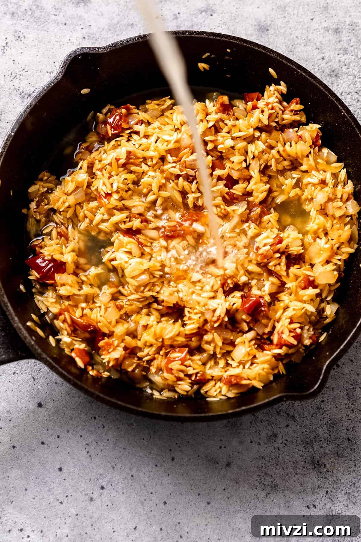 Stock or broth being mixed into the orzo to cook it all in one pot.