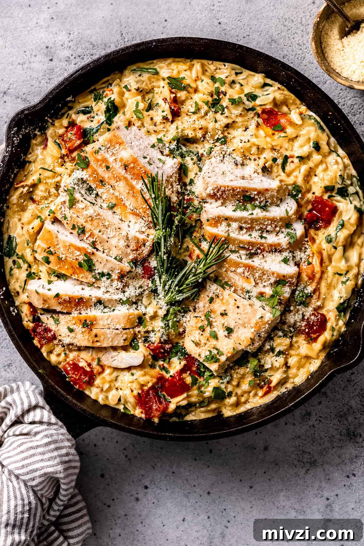 Tuscan chicken and orzo in a skillet with herbs and parmesan cheese.