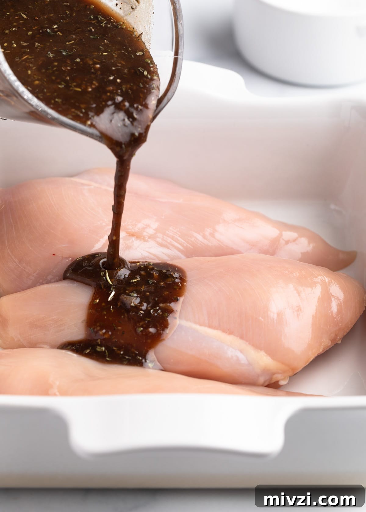 Balsamic-Marinated Chicken Breasts for Juicy Weeknight Meals 5 pouring balsamic marinade over chicken breasts in a white baking dish