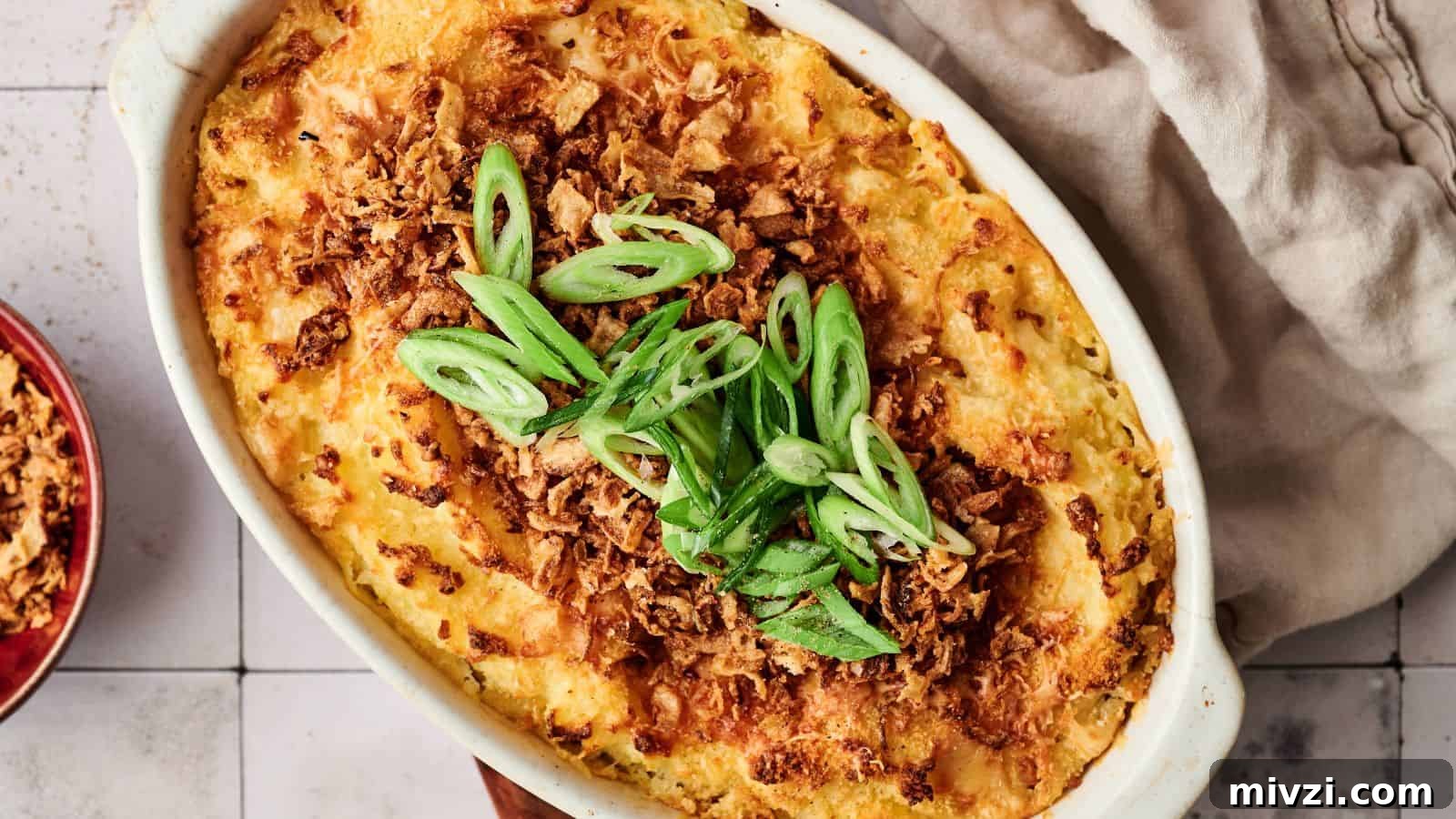 35 Comforting Casserole Recipes to Rely on Tonight 13 A baked casserole topped with crispy fried onions and sliced green onions, served in a white oval dish on a tiled surface with a beige cloth nearby.