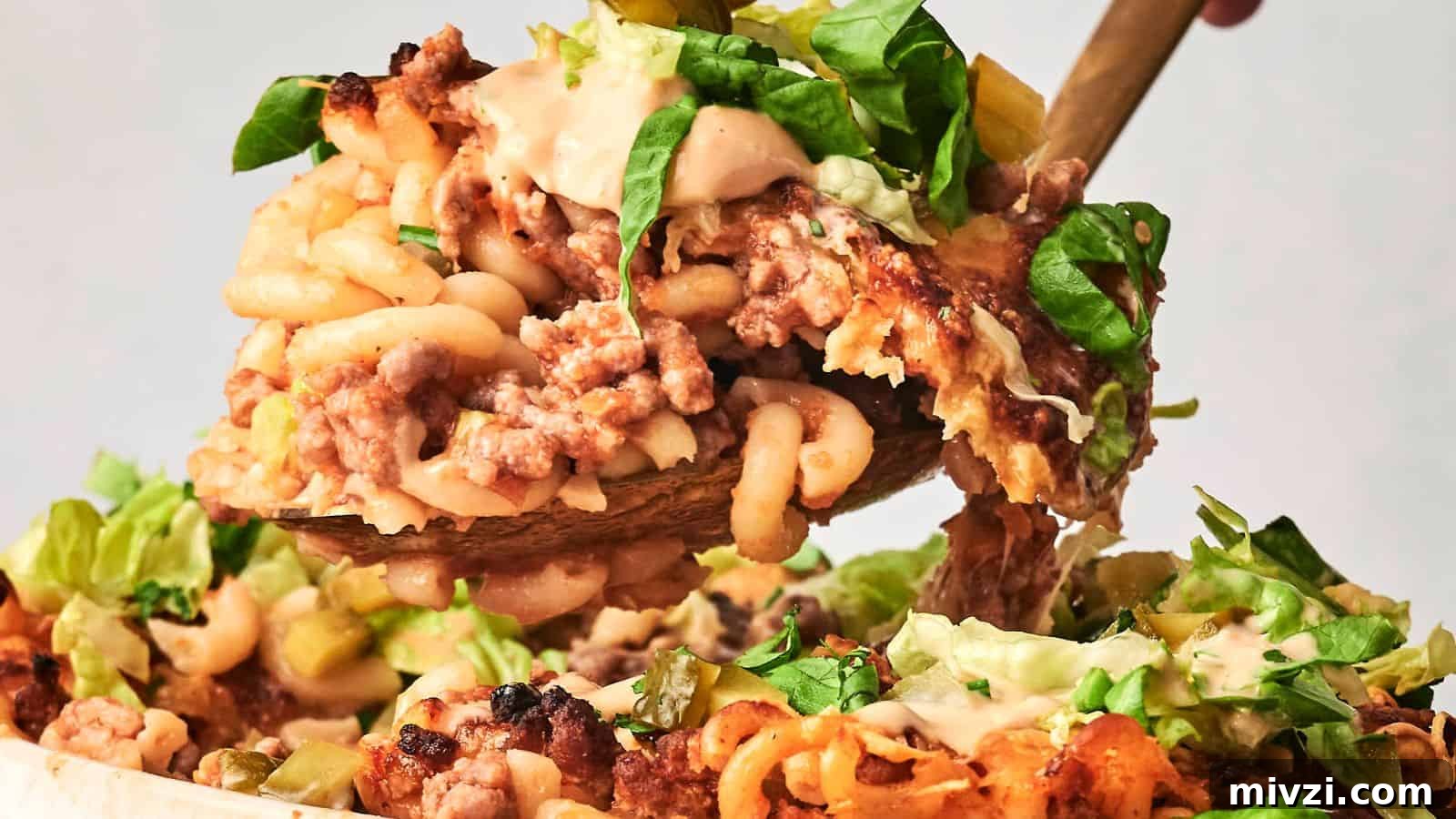 35 Comforting Casserole Recipes to Rely on Tonight 21 A close-up of a spoon lifting a portion of hamburger casserole, showcasing baked macaroni and cheese layered with ground meat and topped with lettuce and creamy sauce.