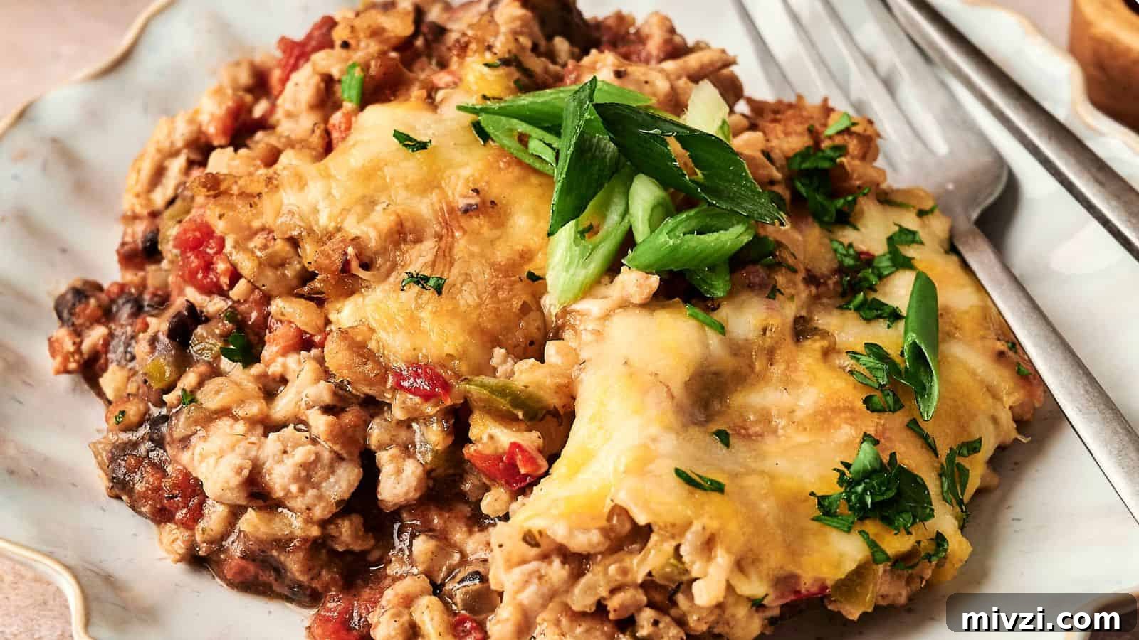 35 Comforting Casserole Recipes to Rely on Tonight 23 A plated serving of cheesy casserole with ground meat, topped with sliced green onions and parsley, accompanied by a fork.