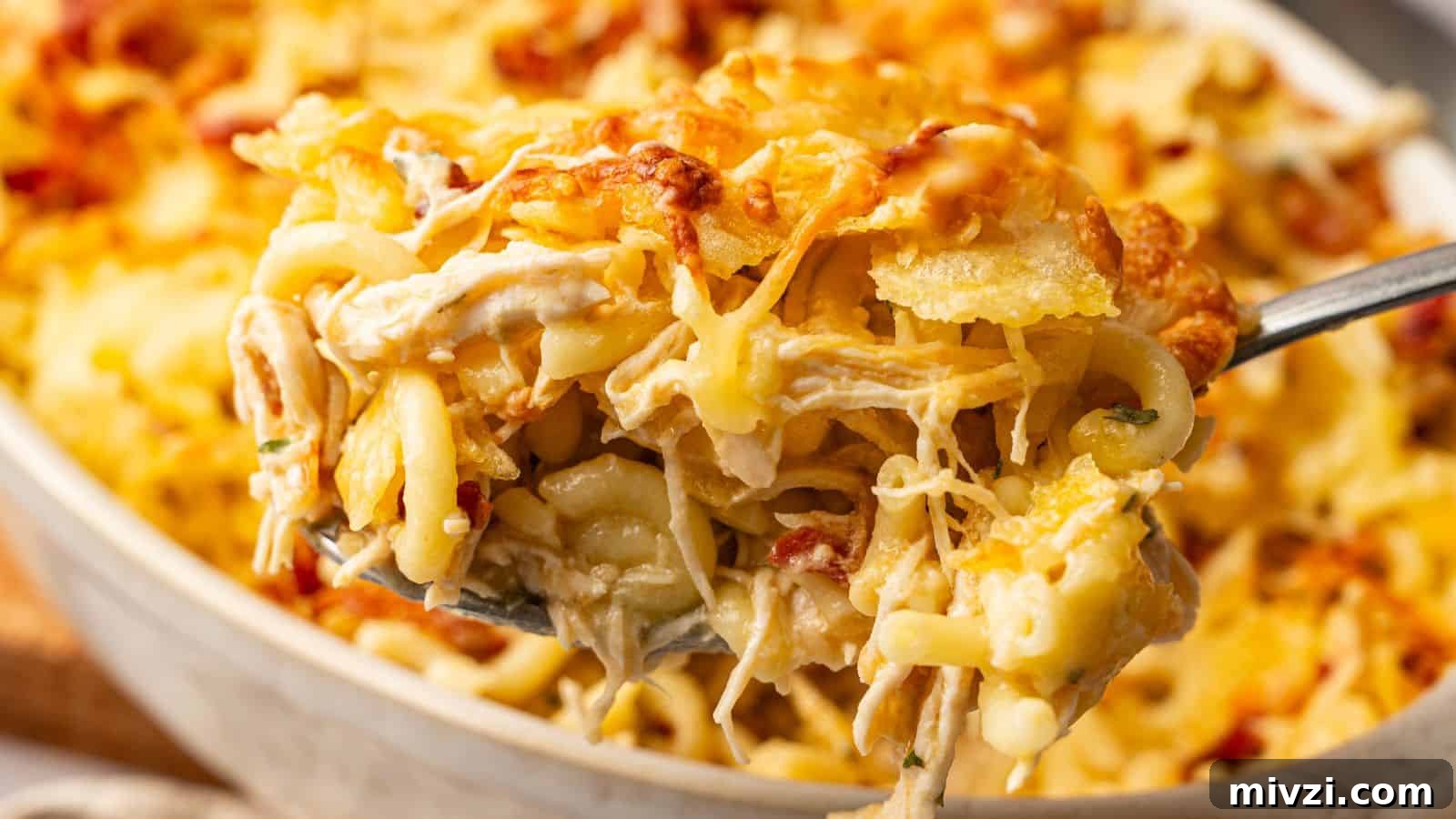 35 Comforting Casserole Recipes to Rely on Tonight 25 A close-up of a spoonful of baked cheesy pasta casserole with shredded chicken and golden melted cheese on top.
