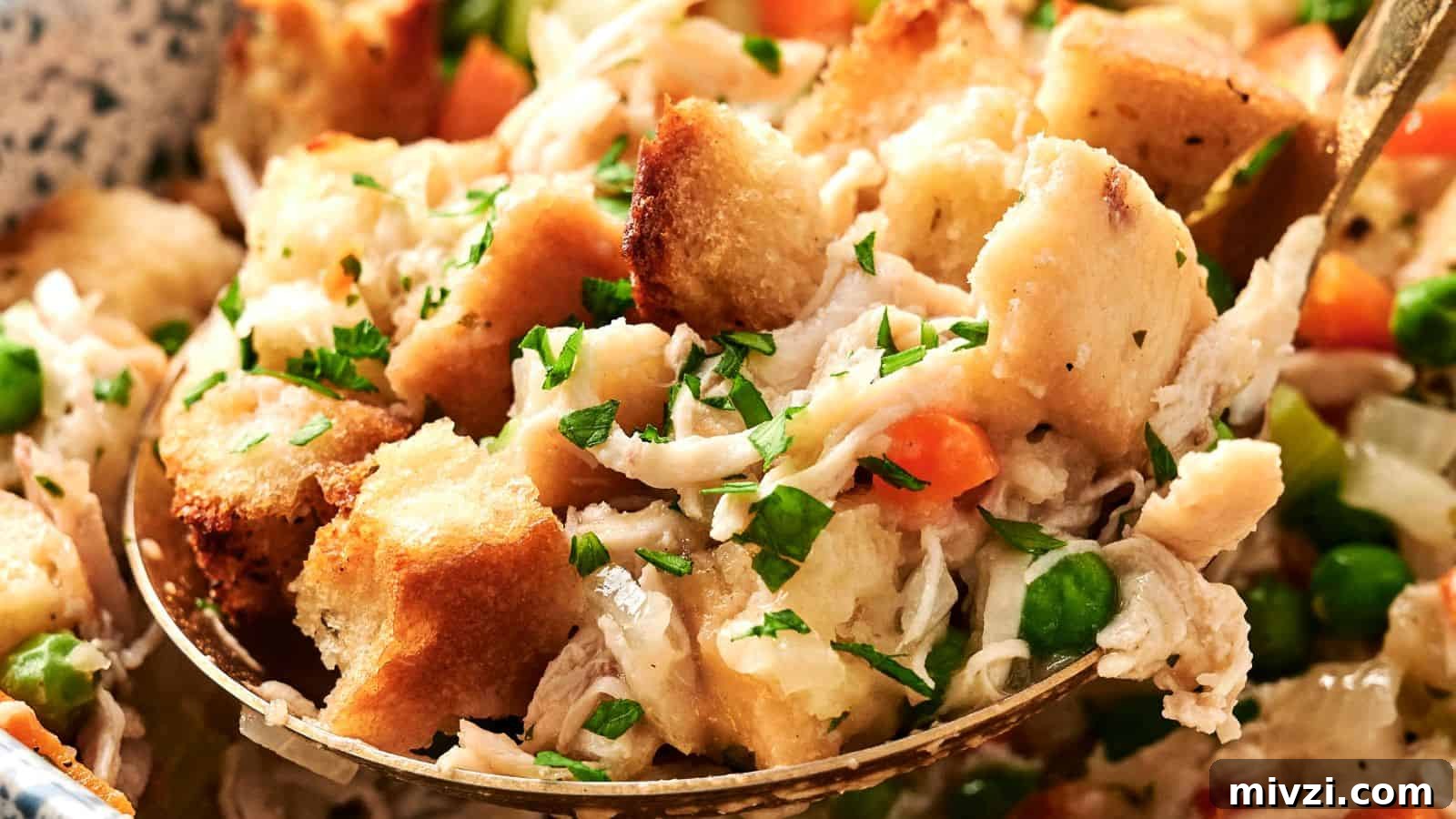 35 Comforting Casserole Recipes to Rely on Tonight 30 A close-up of a spoonful of chicken stuffing, showcasing croutons, shredded chicken, peas, carrots, and sprinkled herbs.