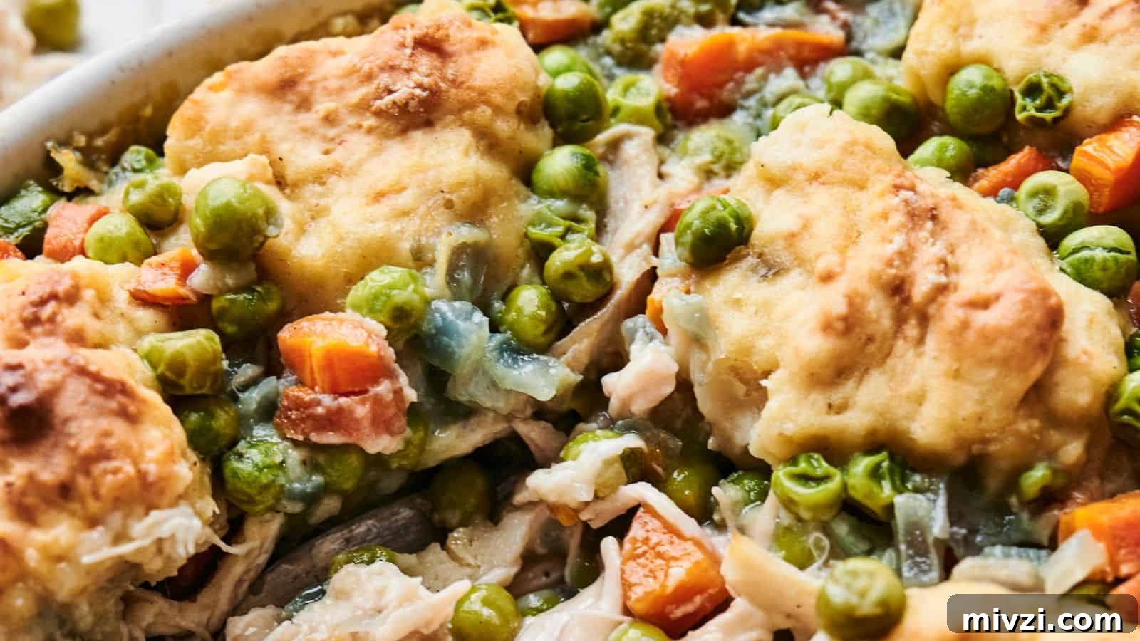 35 Comforting Casserole Recipes to Rely on Tonight 4 Close-up of a chicken and dumpling casserole dish filled with vegetables, including peas, carrots, and chunks of biscuit mixed with tender pieces of meat in a creamy sauce.