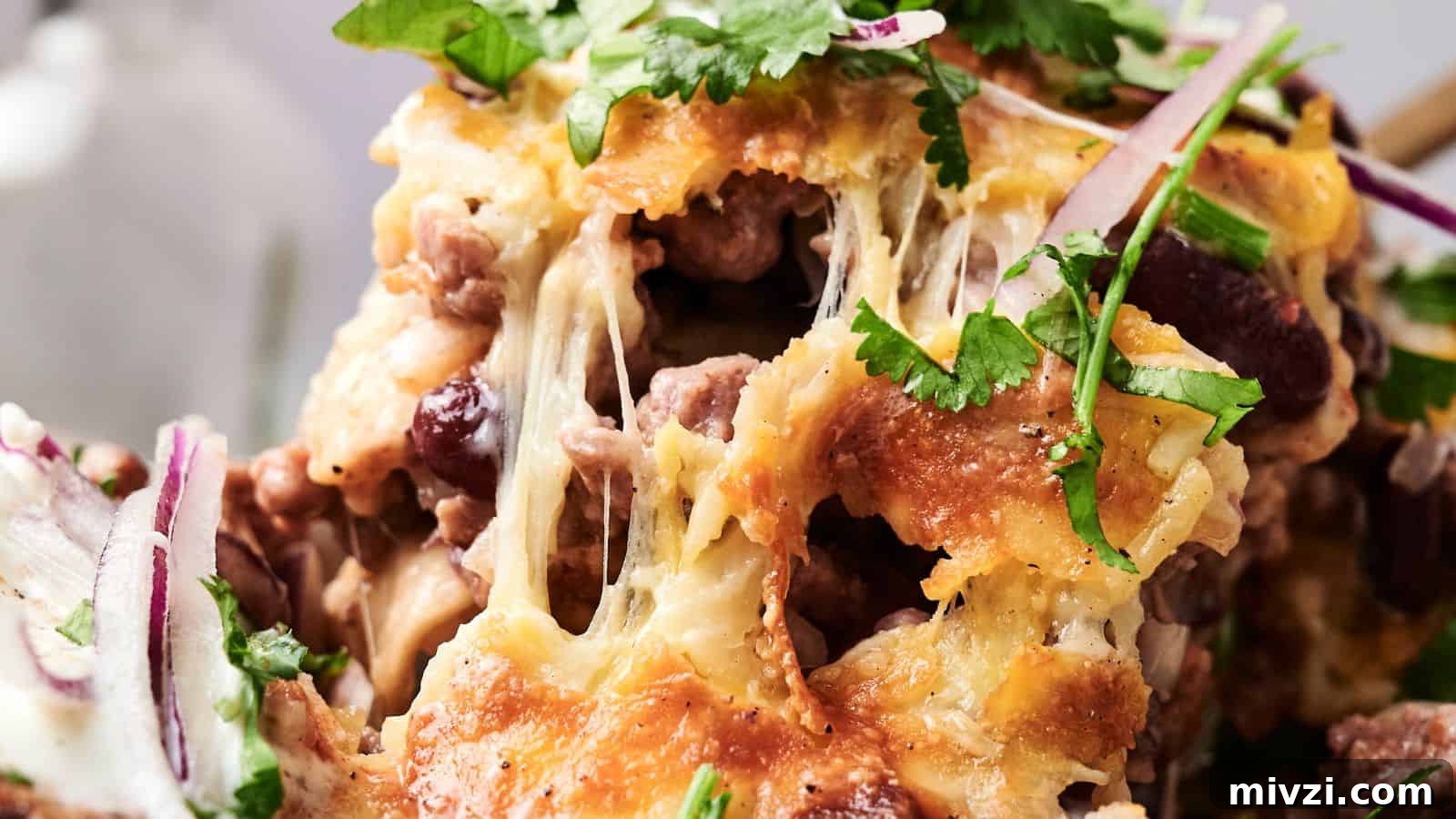 35 Comforting Casserole Recipes to Rely on Tonight 10 Close-up of a cheesy dish with melted cheese, beef, beans, and scattered cilantro leaves. Red onion slices are visible in the foreground.