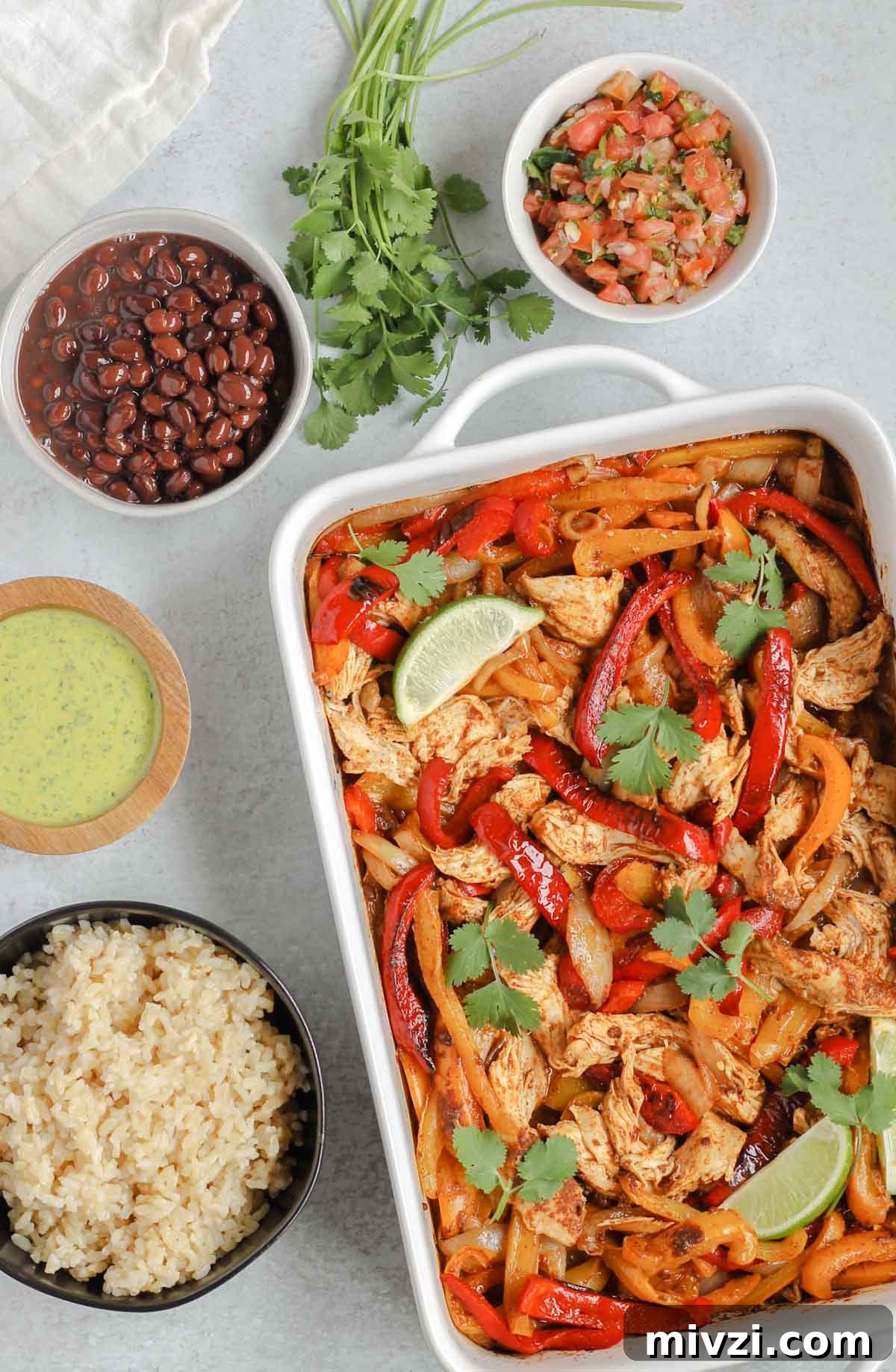 oven baked fajitas in a white baking dish with fajita ingredients in separate bowls around fajita bake