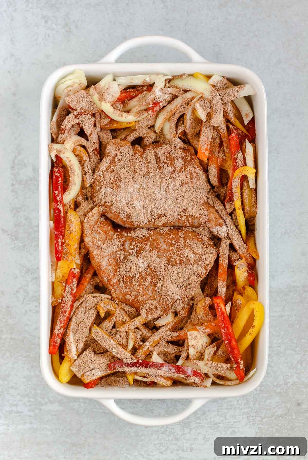 sliced peppers and onions and chicken breasts in a white baking dish