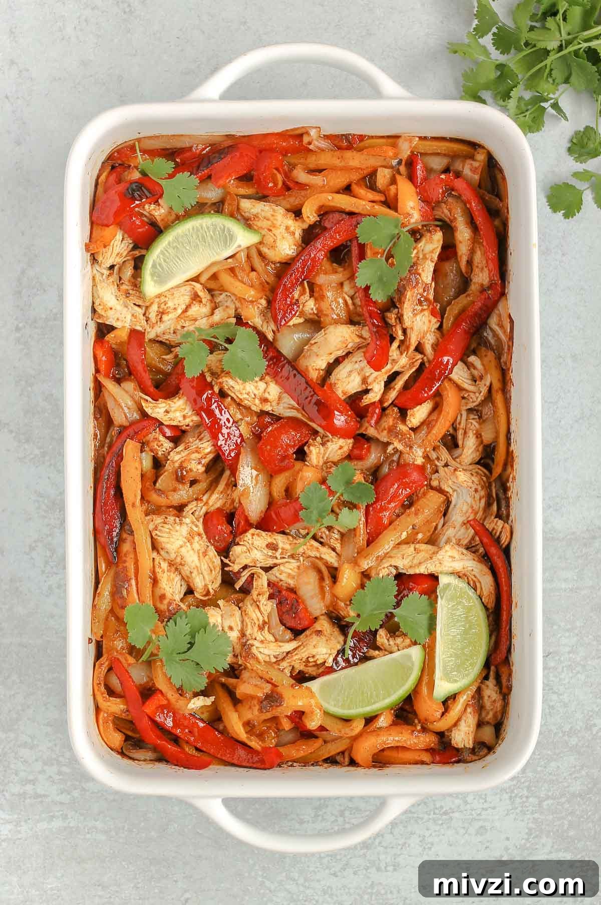 cooked shredded chicken and cooked peppers and onions all mixed together in a white baking dish
