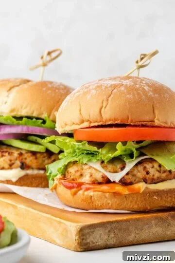 Two air fried turkey burgers with buns on a wood cutting board.