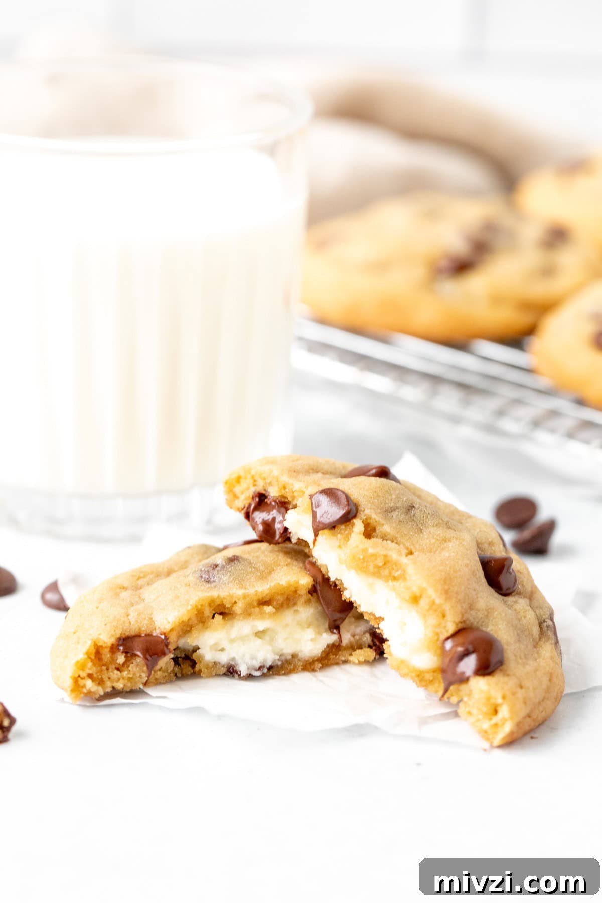cheesecake stuffed chocolate chip cookie, broken in half with glass of milk