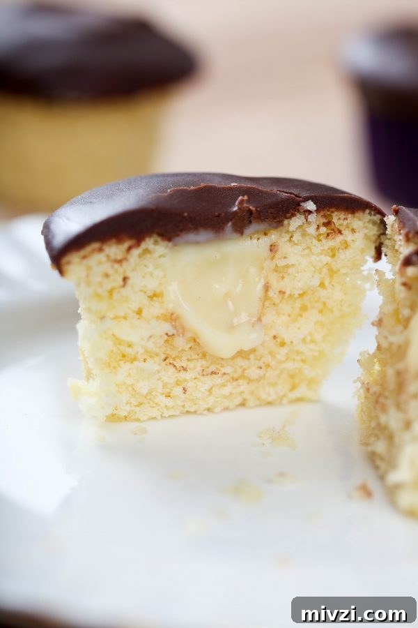 Boston Cream Pie Cupcakes Recipe with Vanilla Custard Filling 2 a Boston cream cupcake cut in half, and filled with pastry cream and topped with chocolate ganache.