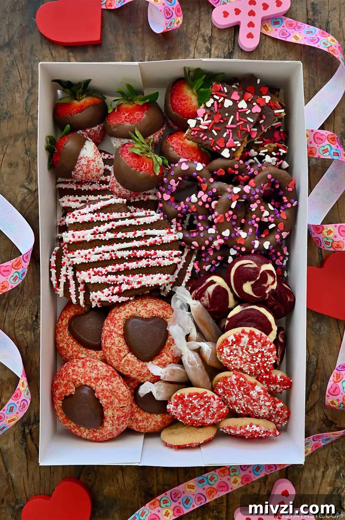 Romantic Valentine’s Day Dessert Ideas and Recipes 4 Valentine's Day dessert box with chocolate sugar cookies, white chocolate-covered strawberries, chocolate-covered pretzels, salted caramels and red velvet cheesecake brownie bites.