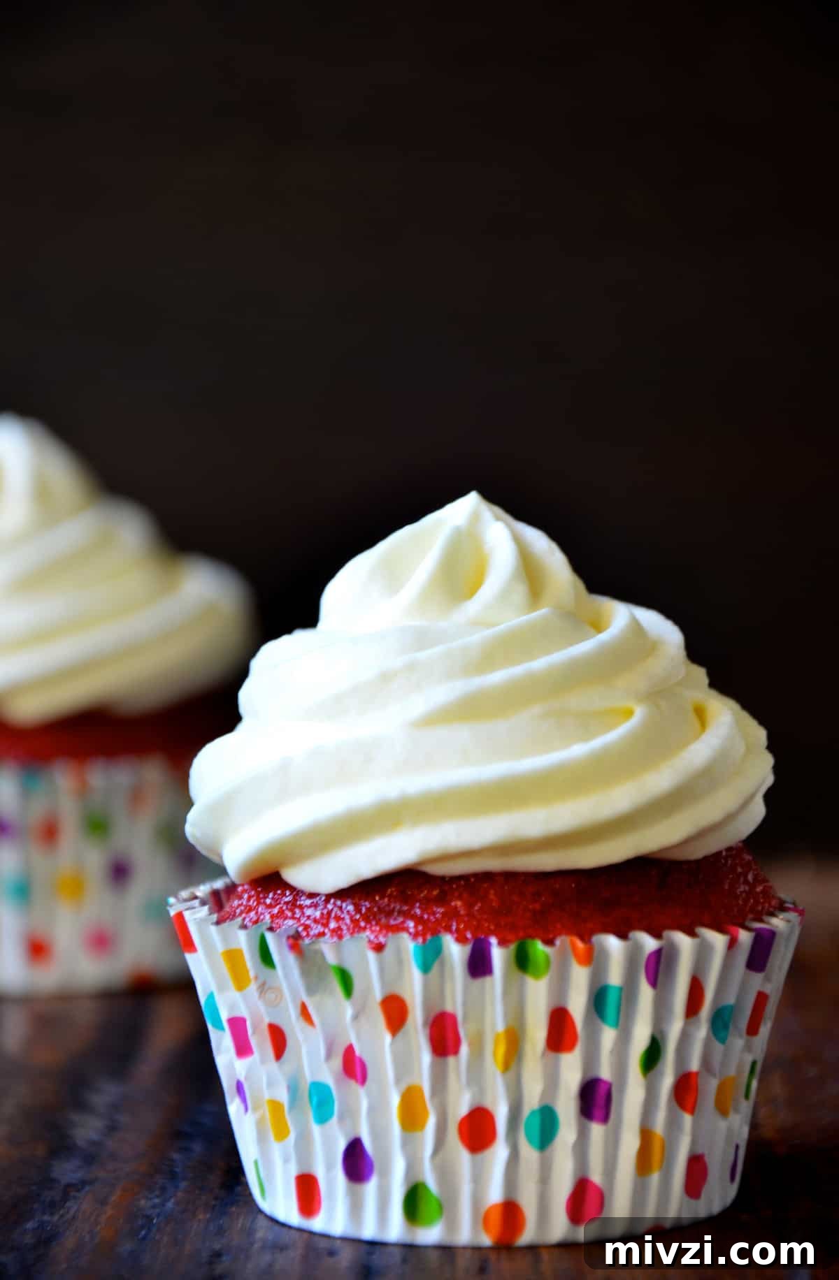 Romantic Valentine’s Day Dessert Ideas and Recipes 5 A red velvet cupcake with cream cheese frosting in a polka-dotted cupcake paper, with another cupcake in the background.