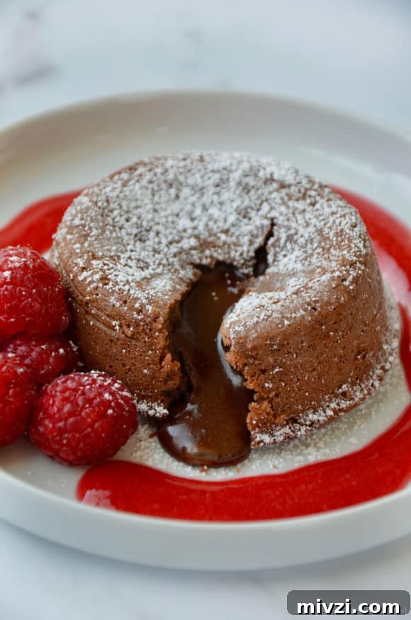Romantic Valentine’s Day Dessert Ideas and Recipes 7 Chocolate Lava Cake on white plate with raspberry sauce and fresh raspberries