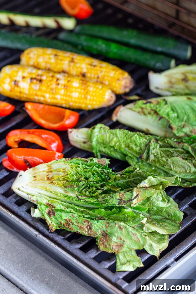 fresh veggies cooking on a grill including romaine lettuce, red bell pepper, corn, and zucchini
