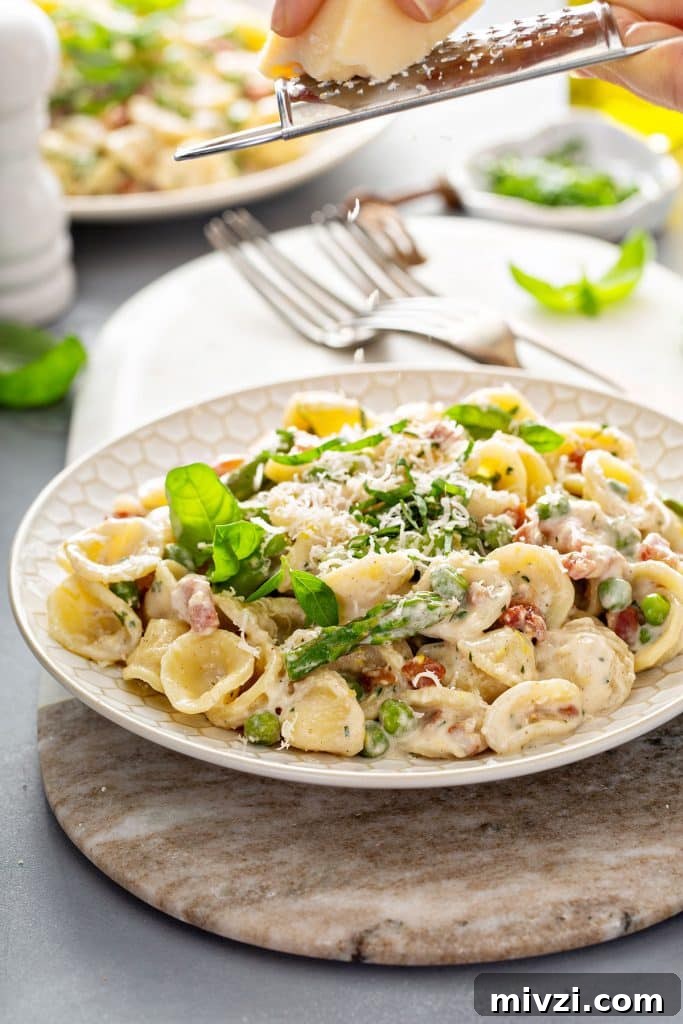 Parmesan cheese getting grated over creamy pasta with asparagus.