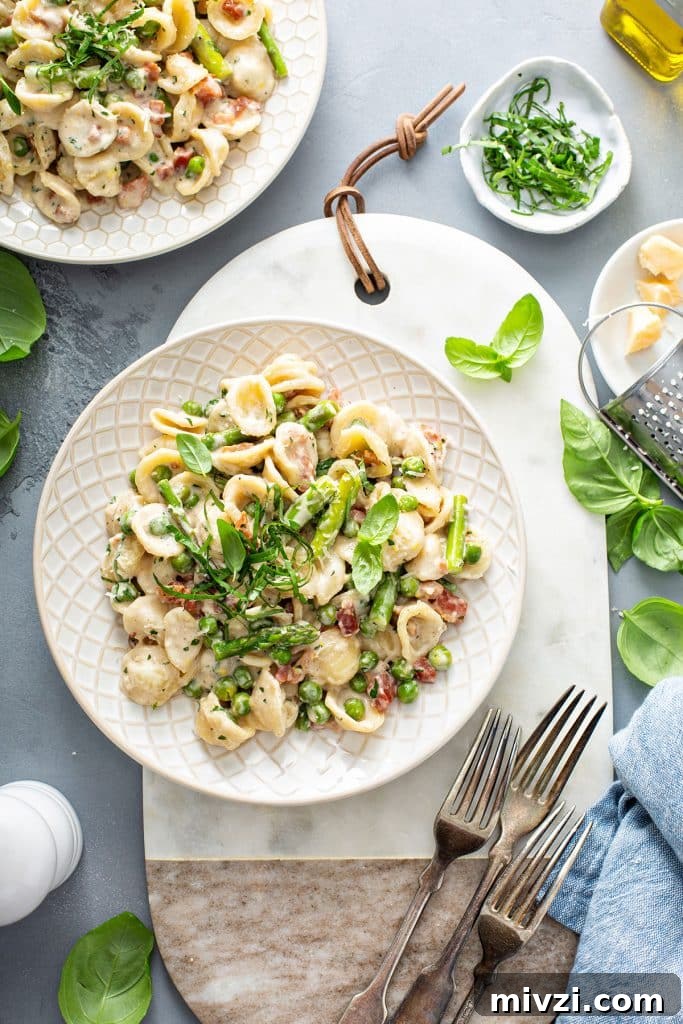 A couple of plates with creamy pasta with asparagus and peas.