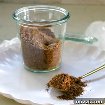 Taco seasoning in a clear glass and on a spoon on a white plate.