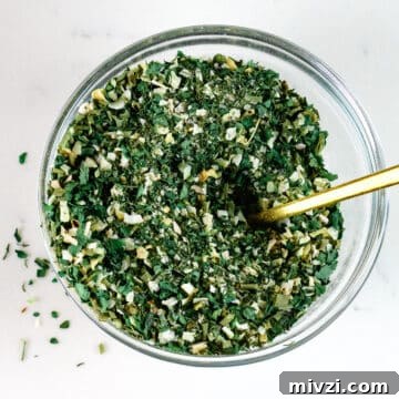 herby seasoning in a small glass dish with gold spoon.