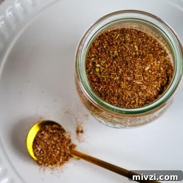 Cajun seasoning in a small weck jar on a white plate with a spoon on the side.