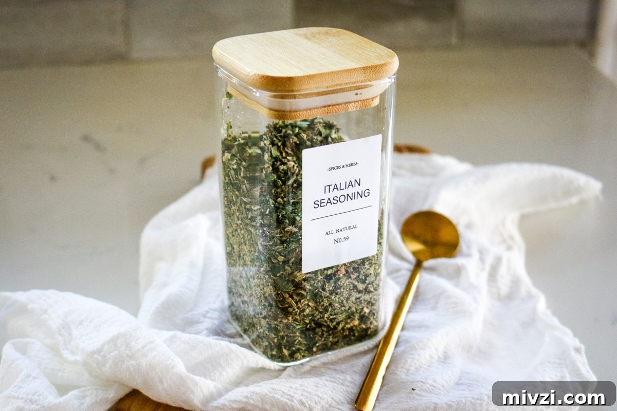 Italian seasoning in a transparent jar, with a spoon next to it.