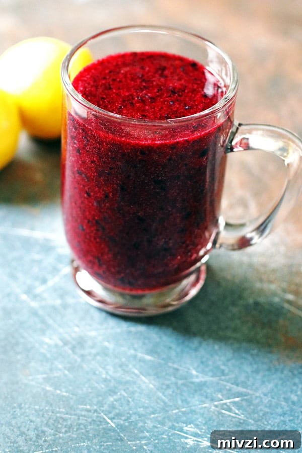Refreshing Blueberry Lemon Smoothie Recipe for Morning Energy 6 Smoothie made of blueberries and lemon in a clear mug. It is sitting on a table with lemons next to it.