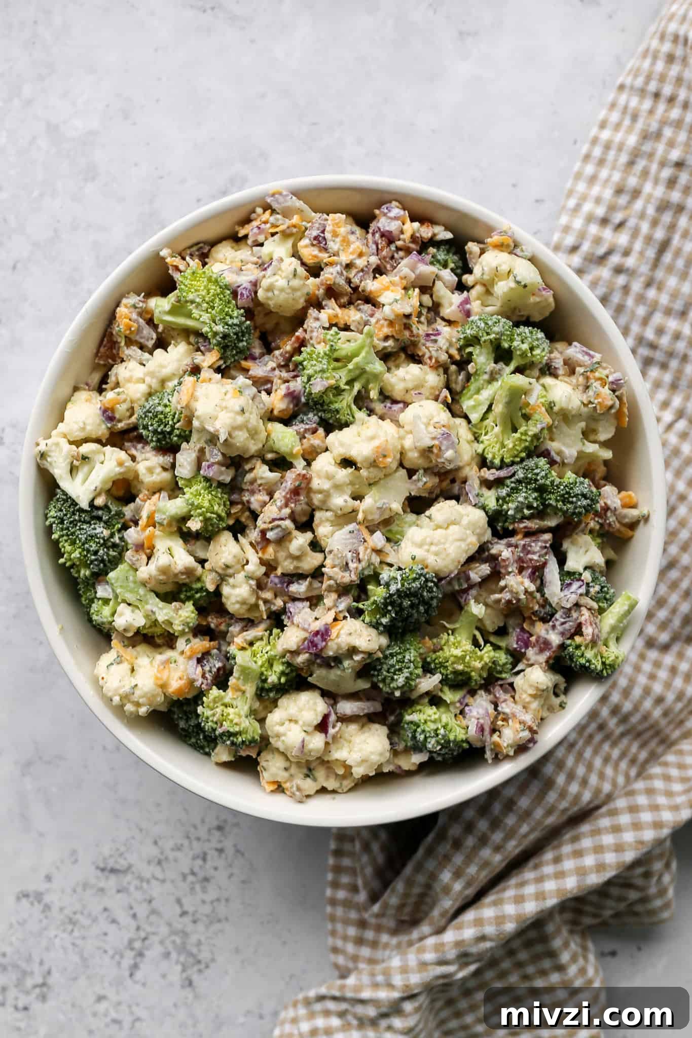 High-Protein Ranch Broccoli and Cauliflower Salad with Chickpeas 3 a bowl of high protein ranch broccoli cauliflower salad next to a tan and white gingham kitchen towel