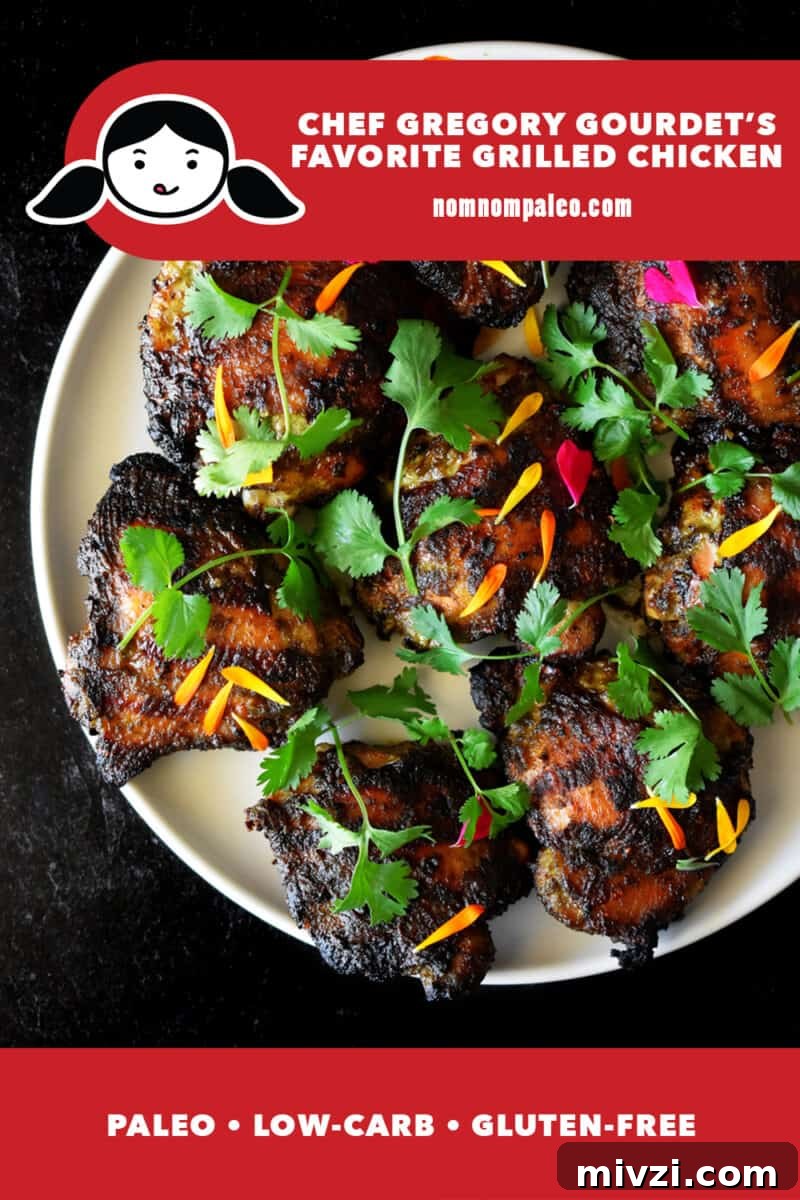 Gregory Gourdet’s Favorite Grilled Chicken Recipe 2 An overhead shot of a round off-white platter topped with grilled chicken thighs and topped with fresh cilantro and edible flowers.