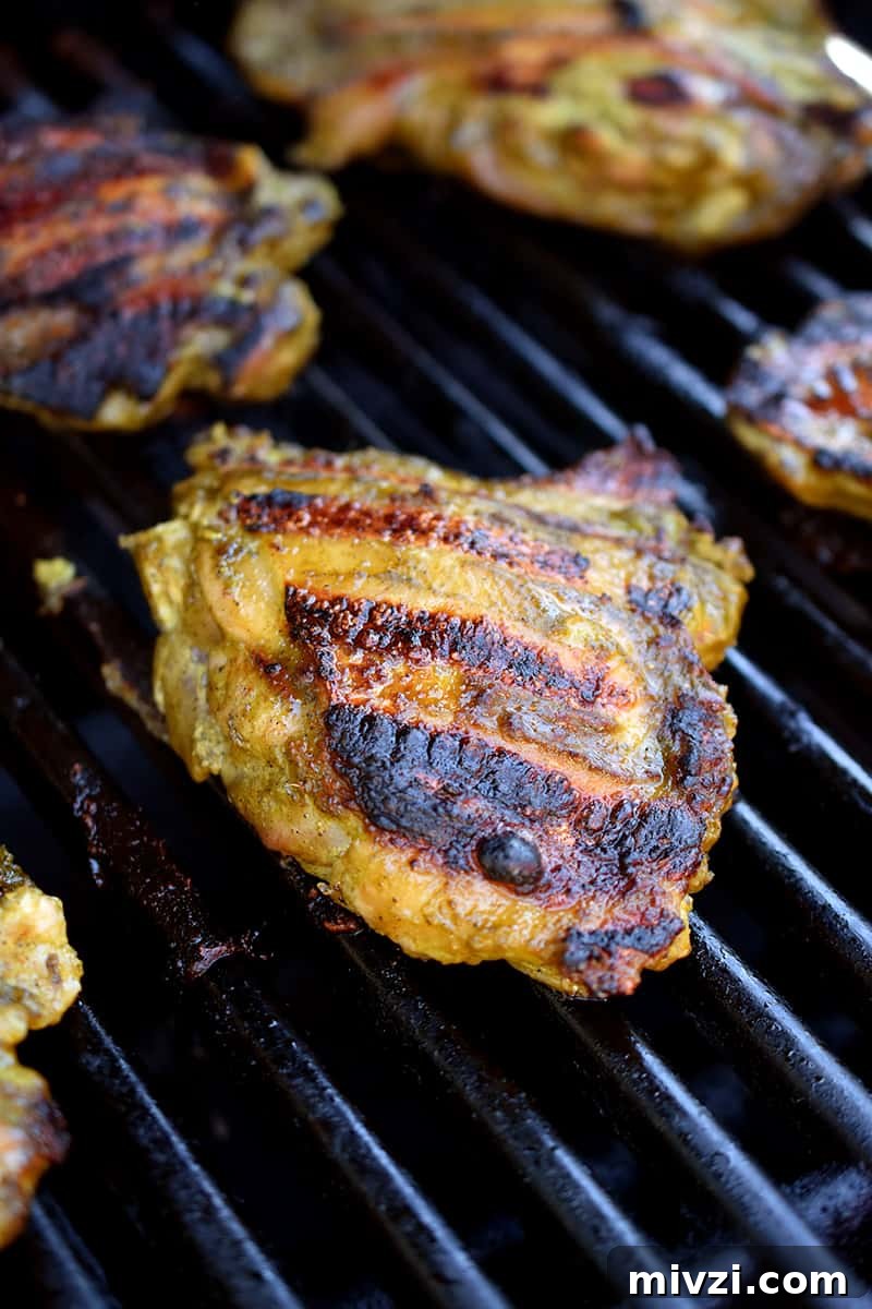 Gregory Gourdet’s Favorite Grilled Chicken Recipe 8 A closeup of chicken thighs on the grill with charred and crispy skin.