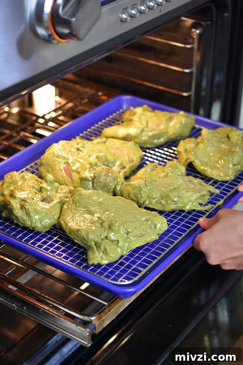 Gregory Gourdet’s Favorite Grilled Chicken Recipe 9 Marinated chicken thighs are on a wire rack in a rimmed baking sheet being placed in an oven