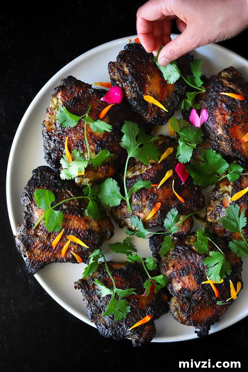 Gregory Gourdet’s Favorite Grilled Chicken Recipe 10 A hand is adding fresh cilantro and edible flower petals to a platter of grilled chicken.