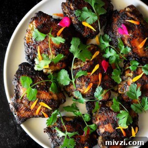 Gregory Gourdet’s Favorite Grilled Chicken Recipe 11 An overhead shot of a round white plate topped with grilled chicken thighs, fresh cilantro, and edible flowers.