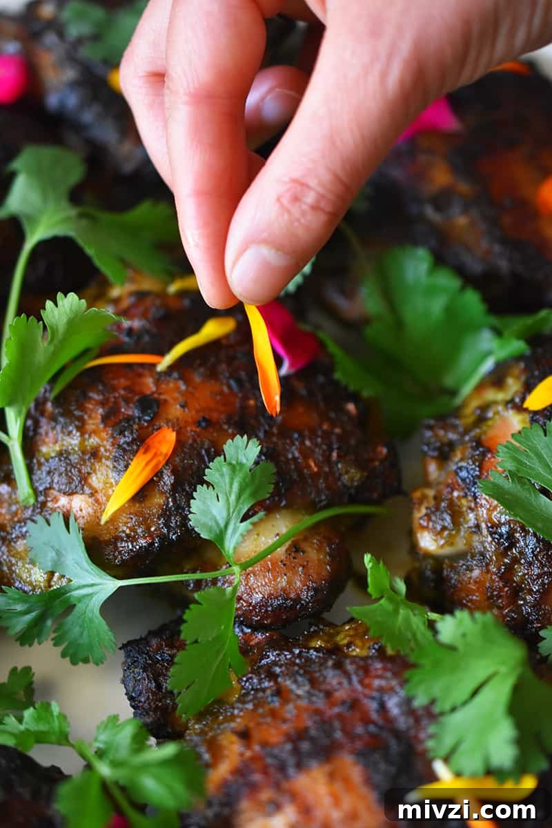 Gregory Gourdet’s Favorite Grilled Chicken Recipe 4 A hand is adding edible flower petals to a platter of grilled chicken with fresh cilantro.