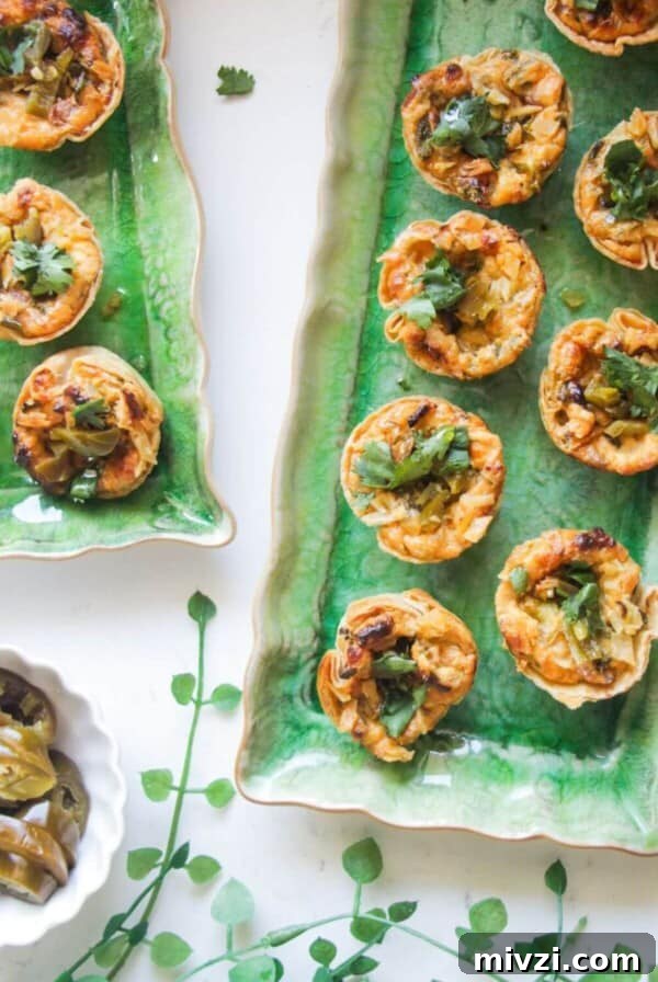 Jalapeno popper taco cups on a green rectangular plate, with a bowl of jalapenos on the side.