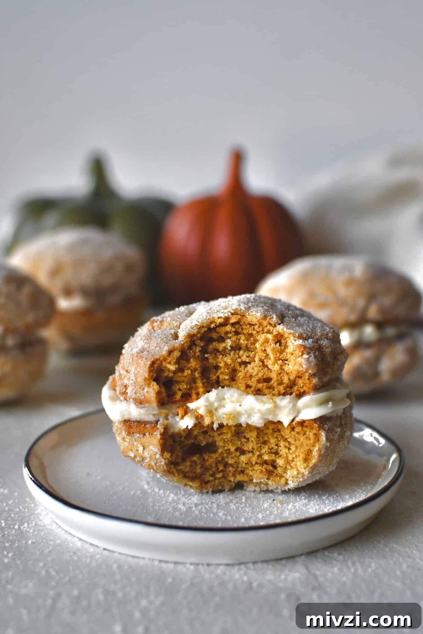 Pumpkin Whoopie Pies Recipe: Soft Spiced Cream-Filled Treats 2 A Pumpkin Whoopie Pie on a plate with a bite taken out of it, surrounded by more whole pies.