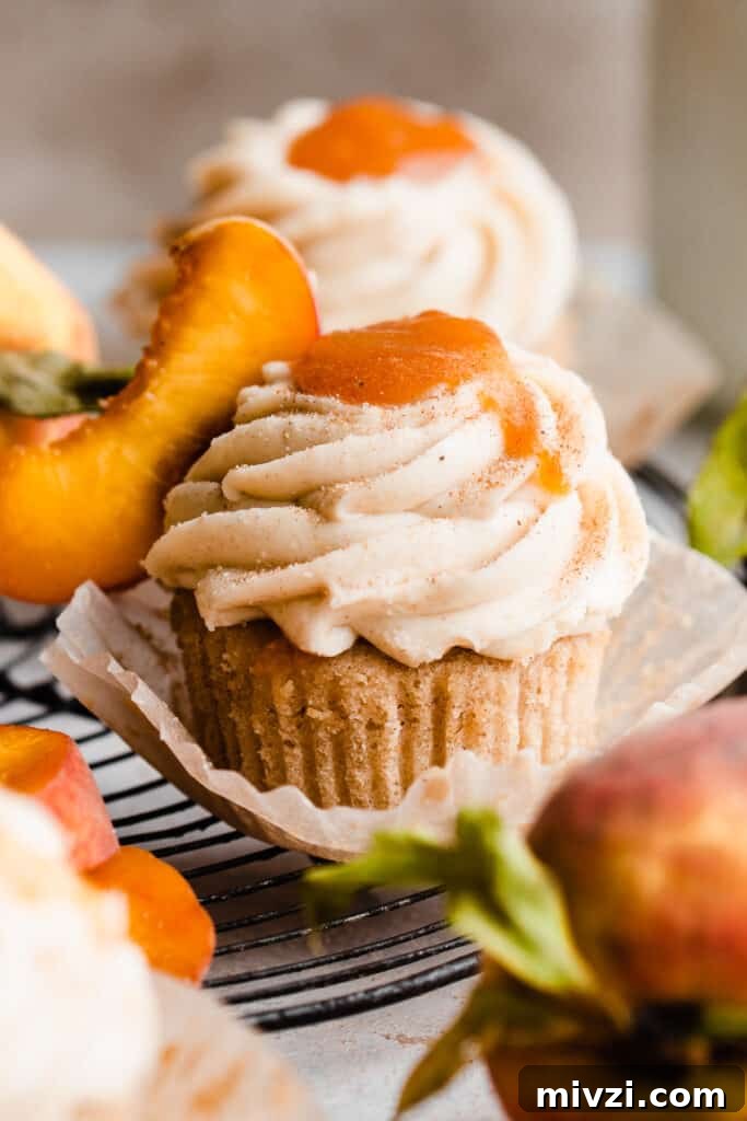 Peach Cupcakes with Cinnamon Cream Cheese Frosting — Summer Dessert Recipe 10 A close-up of a peach cupcake with frosting and peach filling on top.