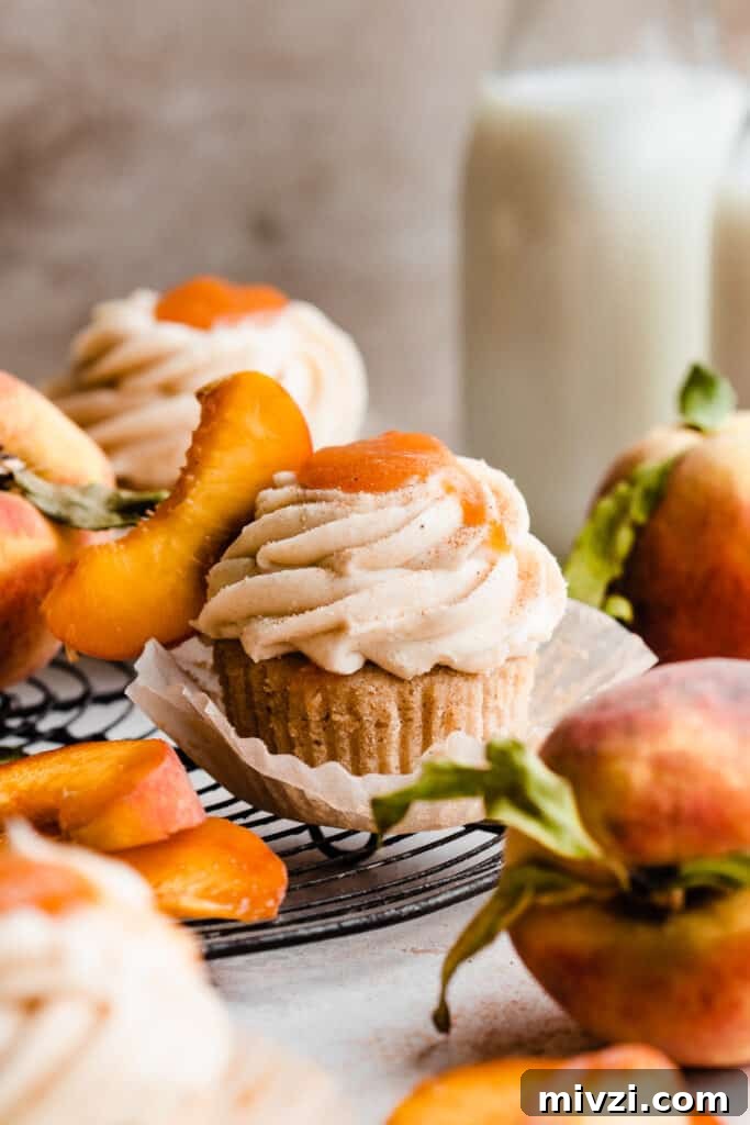 Peach Cupcakes with Cinnamon Cream Cheese Frosting — Summer Dessert Recipe 11 Peach cupcakes on a vintage wire rack with cinnamon cream cheese frosting and peach filling and a fresh peach slice on top.