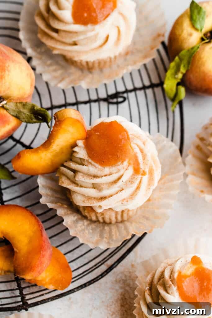 Peach Cupcakes with Cinnamon Cream Cheese Frosting — Summer Dessert Recipe 3 A birds eye view of the peach pie cupcakes on a wire rack, topped with frosting and a dollop of peach pie filling.