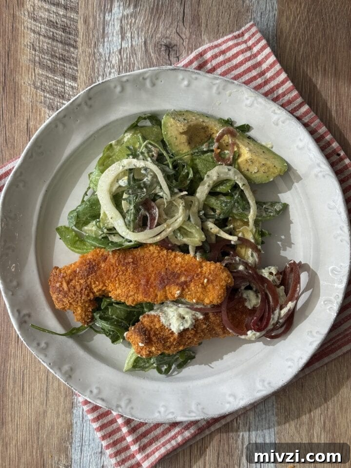 Protein-Packed Baked Chicken Fingers for Muscle Growth 8 baked chicken fingers on a white plate with salad next to it